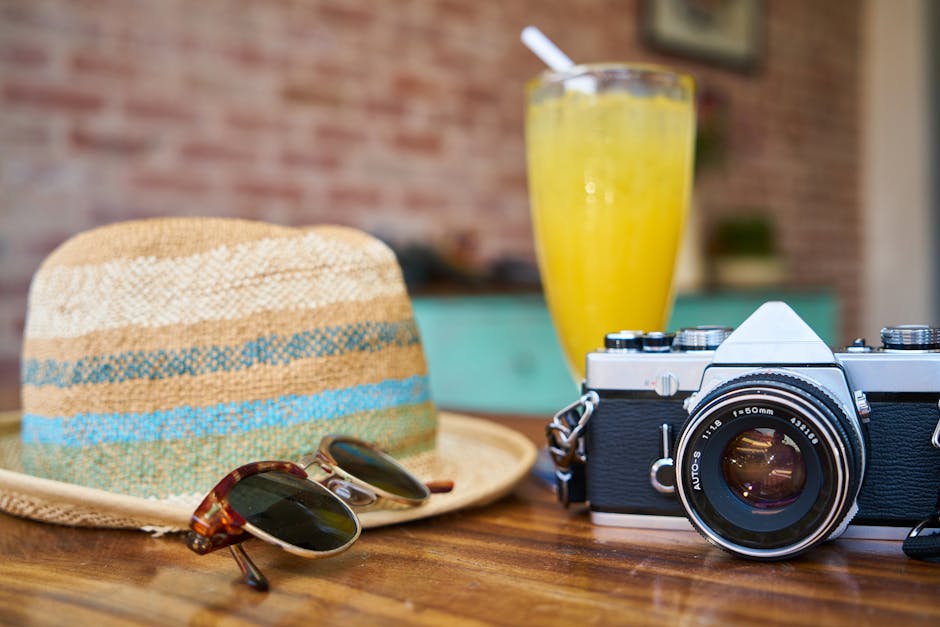 A stylish scene showcasing a vintage camera, hat, and orange juice, evoking summer travel vibes