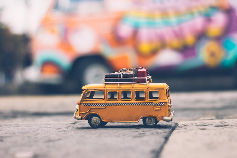 Close-up of a toy Volkswagen van with luggage, set against a colorful street backdrop, evoking summer travel vibes